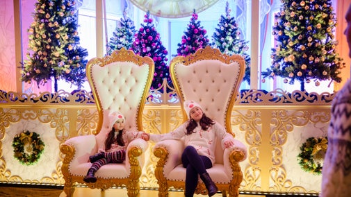 Two children in cream and red Christmas jumpers sitting on huge cream and gold thrones with Christmas trees behind, in Mottisfont's Whistler room for A Cinderella Christmas